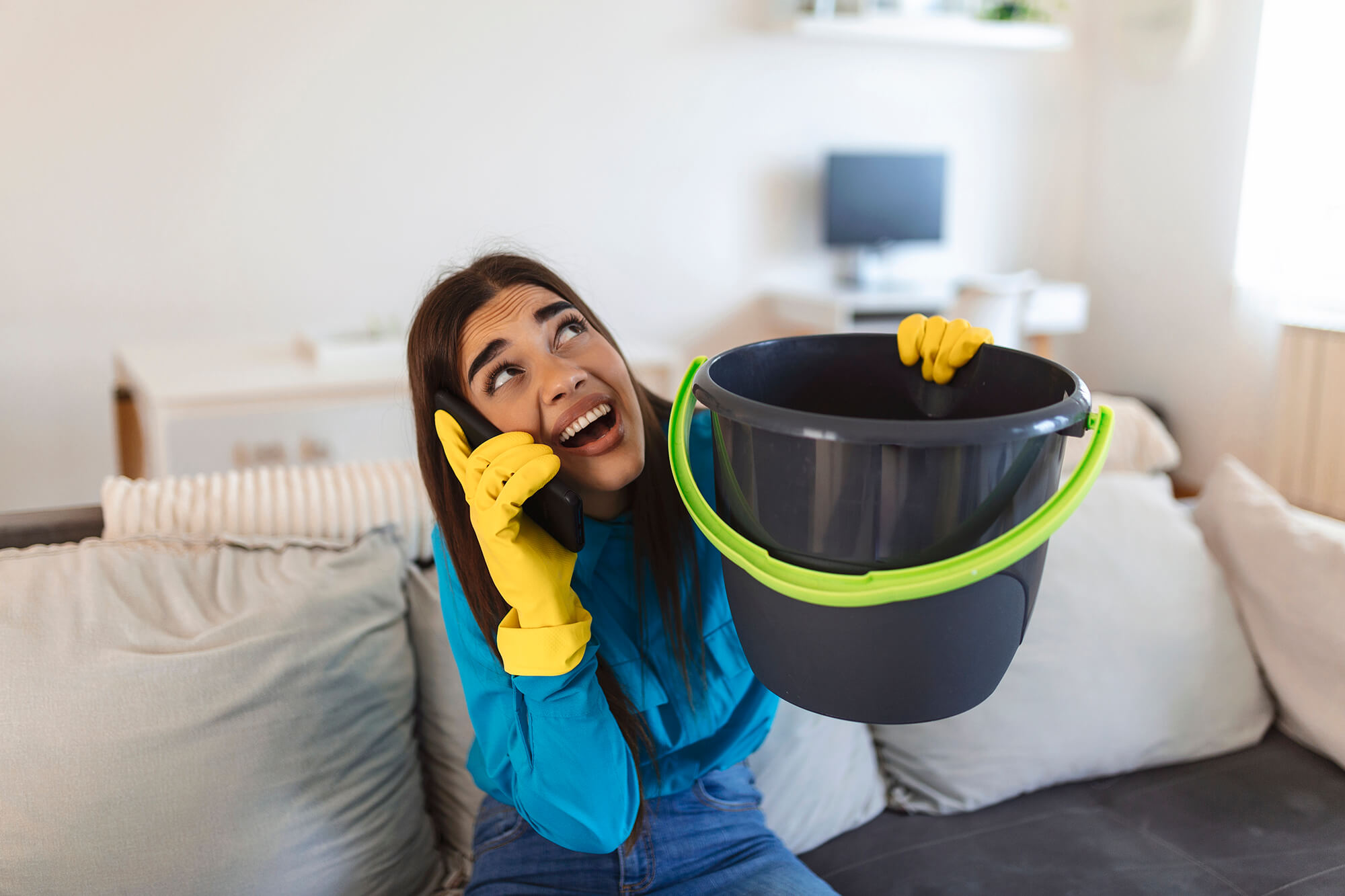femme inquiète appelant plombier tout en recueillant des gouttelettes d'eau qui fuient du plafond à la maison